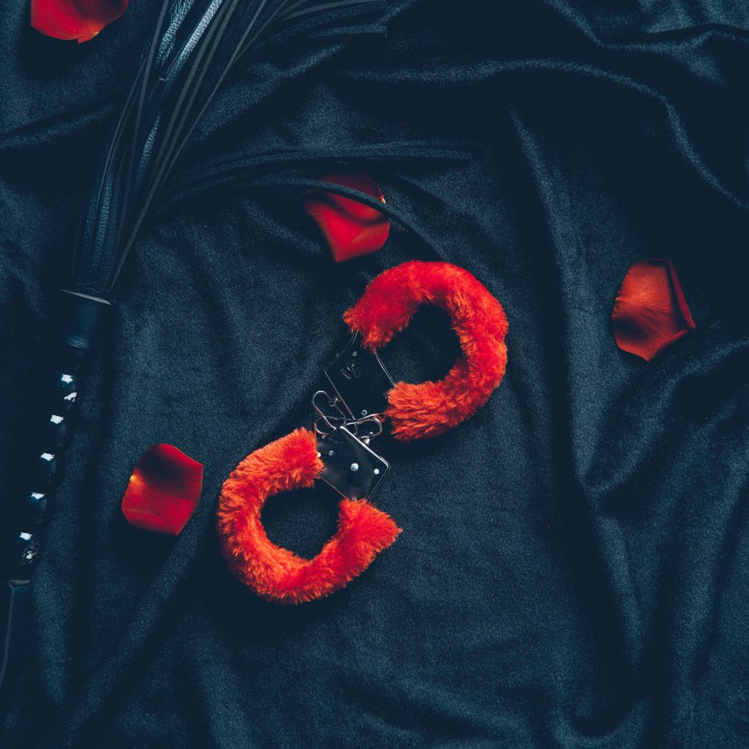 A pair of red fluffy handcuffs and BDSM whip