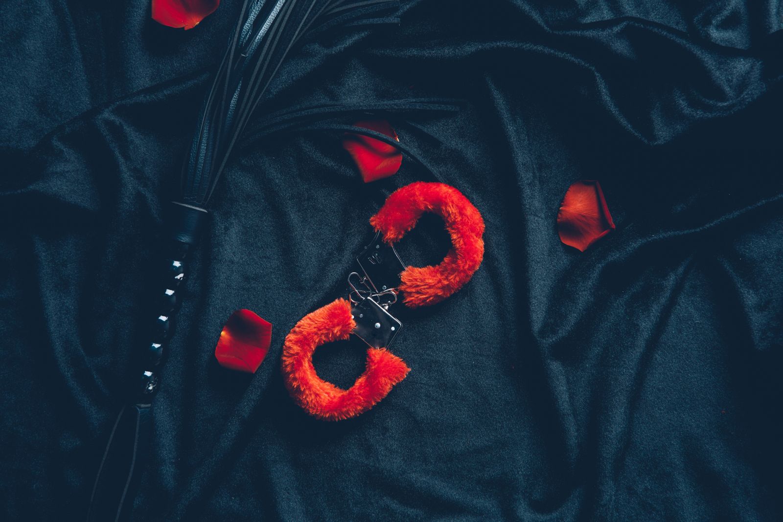 A pair of red fluffy handcuffs and BDSM whip